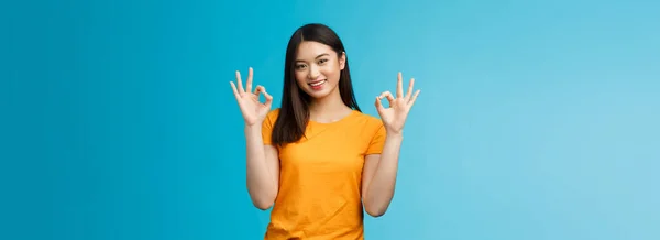 You are perfect. Good-looking cheerful asian girl, show okay ok sign, promote self-acceptance, smiling broadly judging, give positive reply, agree your idea, approve plan, stand blue background.
