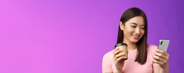 特写友善的亚洲女性博主检查社交媒体喝外卖咖啡 开心地看手机屏幕 阅读有趣的文章 发短信 紫色背景 — 图库照片