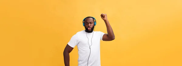 若いアフリカ系アメリカ人の男は身に着けているヘッドフォンとイエローゴールドの上に踊る音楽を楽しむ背景 — ストック写真