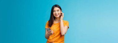 Neşeli, yakışıklı Asyalı kadın mutlu görünüyor, akıllı telefon takılı kulaklık takıyor, gülümsüyor, iyi ses kalitesinden memnun, müzik dinlemekten keyif alıyor mavi arka plan coşkusu.