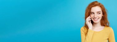 Yaşam tarzı ve teknoloji kavramı - eğlenceli ve heyecan verici arkadaşla cep telefonuyla konuşurken ile neşeli mutlu Kızıl kızıl saçlı kız portresi. Pastel mavi arka plan üzerinde izole. Kopya alanı