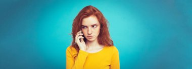Yaşam tarzı kavramı - Kızıl kızıl saçlı kız arkadaşı ile cep telefonuyla konuşurken şok edici ve stresli ifade ile portresi. Pastel mavi arka plan üzerinde izole. Kopya alanı.