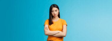 Serious-looking indifferent and upset intense asian woman brunette, cross arms chest look strict ignorant, pissed listening nonsense, annoyed stupid conversation, stand blue background.