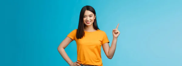 幸せな自信を持ったアジアの女の子自己左上隅を指して 方法を示す 決定笑みを浮かべて 積極的なオンラインストアのプロモーションを導入し 黄色のTシャツの青の背景に立つ保証 スペースのコピー — ストック写真