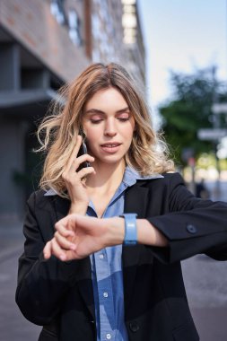 Kendine güvenen bir iş kadınının portresi toplantıya gidiyor, sokakta dikiliyor, cep telefonuyla konuşuyor ve dijital saati kontrol ediyor..