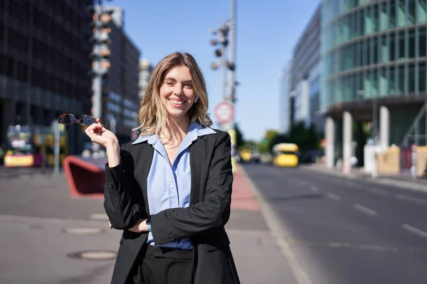 Portrait of successful young company ceo, businesswoman in black suit, standing on sunny street and smiling. Corporate people