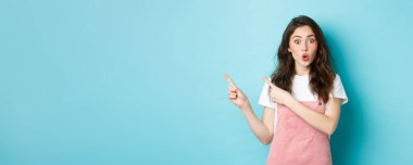 Vay canına, şuna bak. Şaşırmış esmer kadın model dudaklar büzüşüyor ve ilgi çekici görünüyor, parmaklarını ilginç bir şeye doğrultuyor, afiş gösteriyor, mavi arka plan..