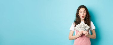 Dolarları tutan, para kazanan, alışveriş yapan, mavi arka plana karşı duran inanılmaz güzel bir kadın model..