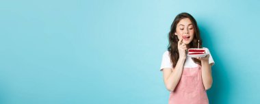 Tatiller ve kutlamalar. Tatlı doğum günü kızı ısırmak için nefis pastalara bakıyor, mavi arka planda hayaller kuruyor..