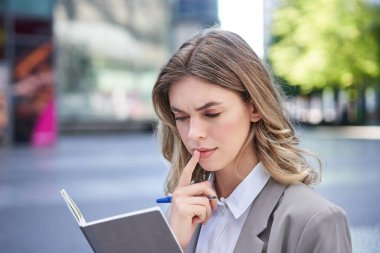 Kadın notlarını okurken konsantre oluyor, röportaj için hazırlanıyor. Takım elbiseli iş kadını deftere yazıyor, şehir merkezinde oturuyor..