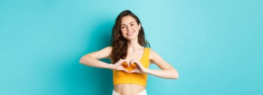 Yaz tatili ve duygu konsepti. Genç romantik kız seni sevdiğimi gösteriyor. Kalp hareketi, gülümseme, mavi arka planda durmak..