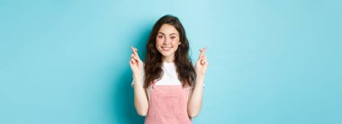 Umut dolu esmer kızın gülümsemesi, şans için dua etmesi, dua etmesi ya da umut etmesi, mavi arka planda durması..