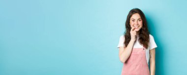 Sevimli kız bir şeyler denemek ve tatmak istedi, parmağını ısırmak ve gülümsemek, kameraya arzu ve ilgiyle bakmak, ürüne bakmak, mavi arkaplana karşı durmak..