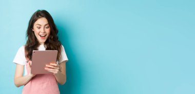 Heyecanlı genç kadın görüntüsü dijital tablet ekranda şaşkınlık içinde, mavi arkaplana karşı duran harika bir şey buldu..