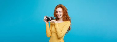 Seyahat ve insanlar kavramı - mutlu ifade vintage fotoğraf makinesi ile oynarken mutlu Kızıl kızıl saçlı kız portresi Headshot. Pastel mavi arka plan. Kopya alanı.