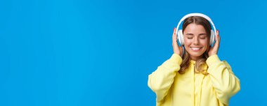Müzik, yaşam tarzı ve gençlik kavramı. Rüya gibi mutlu ve rahat Avrupalı genç bir kızın yakın plan portresi. Gözlerini kapat ve kulaklıkla şarkının güzel sesini dinle, hayal kur, mavi arka plan..