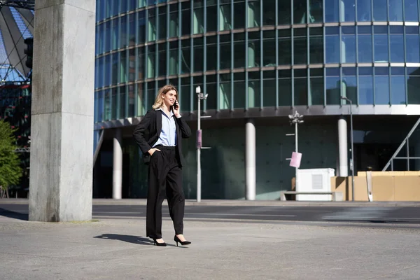 スーツを着た若い企業の女性が通りを歩き 携帯電話で話しています 仕事中に電話で話をするビジネスマン ロイヤリティフリーのストック画像