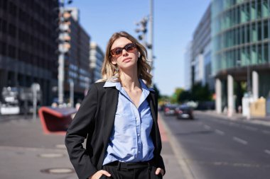 Takım elbiseli ve güneş gözlüklü kadın portresi, sokakta duruyor, kendinden emin ve rahat görünüyor..