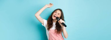 Güzel bayan şarkıcı mikrofon tutuyor, mikrofonda karaoke söylüyor, mavi arka planda duruyor..