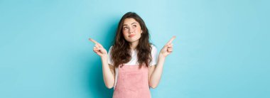 Kararsız güzel kız düşünür, seçimini yapar, sol ve sağ tarafı işaret eder ve omuz silker, ne seçeceğini ya da alacağını bilmez, mavi arka planda durur..