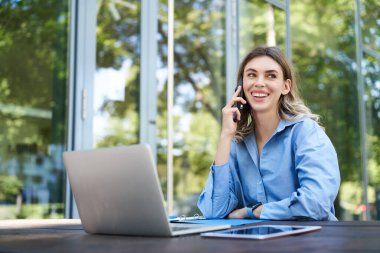 Ofis binasının yakınındaki temiz havada çalışan satış elemanının portresi. Bilgisayarlı gülümseyen şirket kadını, telefon görüşmesi yapıyor..
