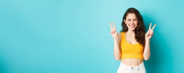 Yaz tatili ve duygu konsepti. Sevimli kız gülümseyip gülüyor, mavi arka planda barış işaretleri gösteriyor..