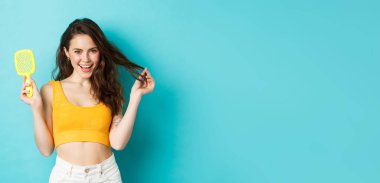 Mutlu, çekici bir kadın saç teli olmadan fırçasını gösteriyor ve uzun, sağlıklı bir saç stiline dokunuyor. Mutlu bir yüzü var. Şampuan sonuçlarından memnun, mavi arka plan..