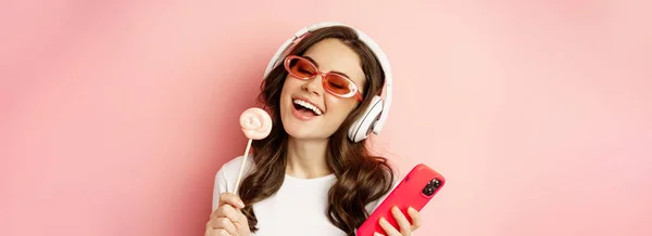 Beautiful Female Model Listening Music Headphones Holding Lolipop Mobile Phone — Zdjęcie stockowe