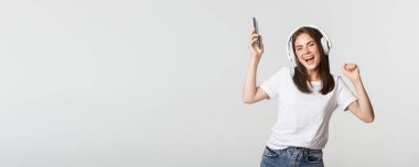 Güzel esmer kız dans ediyor ve kablosuz kulaklıkla müzik dinliyor, elinde akıllı telefon tutuyor..