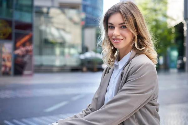 Portrait of smiling woman in office suit, sitting outdoors, looking confident.