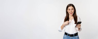 Tutkulu kız akıllı telefonu işaret ediyor ve gülümsüyor, internette büyük indirimler gösteriyor, cep telefonunda uygulama kullanıyor, beyaz arka plan.