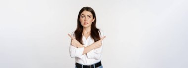 Indecisive adult woman pointing fingers sideways hesitant, making choice between two variants, standing over white background.