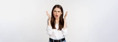 Frustrated and angry young woman gasping, looking shocked and upset at camera, offended by smth, standing bothered against white background.