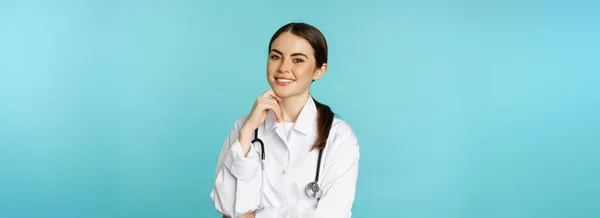 医療スタッフと医師のコンセプト 若い笑顔の女性医師 白いコートと聴診器の医療従事者 自信を持って待っている患者 青い背景を見て — ストック写真