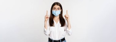 Coronavirus 'tan gelen tıbbi maskeli kurumsal bir kadının portresi, işaret eden, reklam veren, beyaz arka plan.