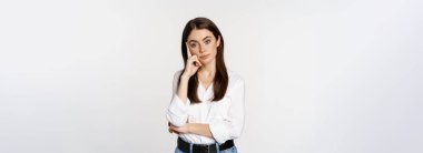 Unamused, bored brunette woman looking gloomy and sad, sighing, standing reluctant over white background.