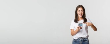 Heyecanlı ve mutlu esmer kız akıllı telefon ekranını işaret ediyor..