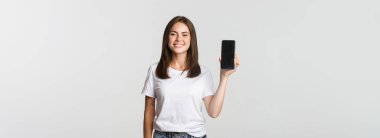 Çekici gülümseyen genç bayan memnun görünüyor, akıllı telefon ekranı gösteriyor..