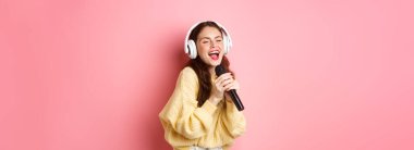 Kaygısız kız karaoke gecesinden zevk alıyor, mikrofonda şarkı söylüyor, kablosuz kulaklık takıyor, pembe arka planda duruyor..
