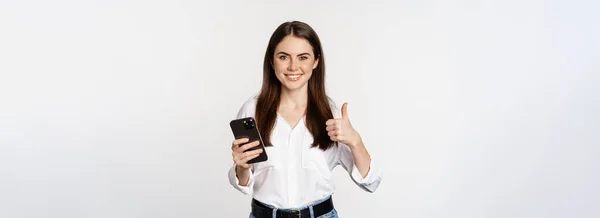 快乐微笑的企业女性 展示大拇指的女性模特 手持智能手机 使用手机 站在白色背景之上 — 图库照片