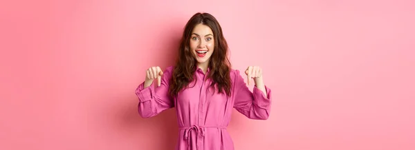 ピンクの背景を背景に立って プロモーションオファーをチェックアウト 幸せと面白がって見て 指を指してスタイリッシュな服で興奮した笑顔の女性 — ストック写真