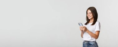 Güzel, gülümseyen bir kız cep telefonu kullanıyor, akıllı telefona bakıyor..