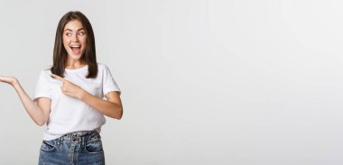 Çekici genç bir kadın elinde tuttuğu bir şeyi işaret ediyor..