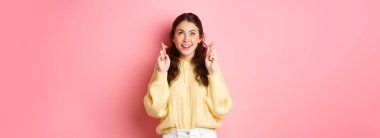 Sevimli kız öğrenci sınavı geçmek istiyor, şans diliyor, yukarı bakıyor ve dua ediyor, iyimser gülümsüyor, pembe arka planda duruyor..