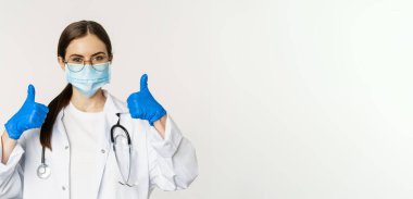 Coronavirus 'un yüz maskesi takmış kadın doktorların portresi. Baş parmaklarını gösterip gülümsüyor. Klinik ya da tıbbi web sitesi tavsiye ediyor..
