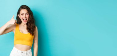 Yaz tatili ve duygu konsepti. Neşeli genç bir kadın evet diyor, iyi seçimi övüyor, iyi iş çıkarıyor, başparmaklarını kaldırıyor ve heyecanlı görünüyor, mavi arka planda duruyor..