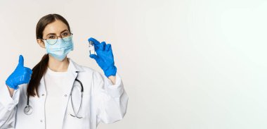 Profesyonel doktor, tıbbi maske ve gözlüklü doktor, aşıyı gösteren ve onaylayan, covid-19 'dan aşı olmayı öneren genç kadın portresi..