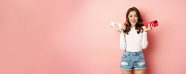 Technology, spring promo concept. Stylish glamour woman holding two smartphones, mobile phones in both hands, smiling pleased, buying new cellphone, pink background.