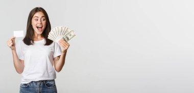 Paraya bakan, elinde kredi kartı olan, beyaz arka planda duran güzel bir kız..