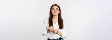 Young moder business woman, office lady holding mug with coffee tea and smiling, standing against white background.